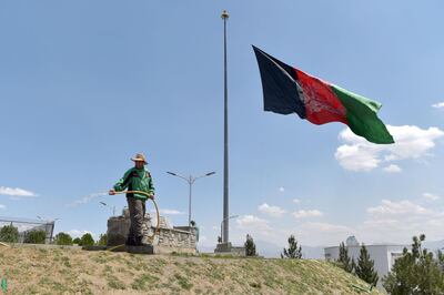 A worker waters a lawn near an Afghan national flag flying at half-mast in Kabul on May 11, 2021 during a national day of mourning announced by Afghan President Ashraf Ghani to condemn the recent terrorist attacks. / AFP / WAKIL KOHSAR
