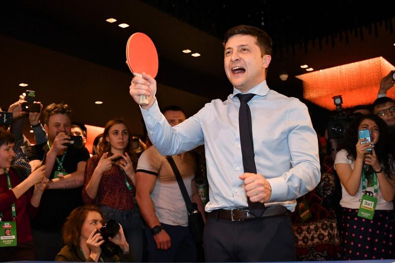 TOPSHOT - Ukrainian comic actor, showman and presidential frontrunner Volodymyr Zelensky surrounded by cameramen and photographers plays table tennis with a journalist ahead of the provisional results at the headquarter in Kiev on March 31, 2019. Comedian and political novice Volodymyr Zelensky topped the first round of Ukraine's presidential election on Sunday, exit polls showed, leading incumbent Petro Poroshenko into a run-off.  / AFP / Genya SAVILOV
