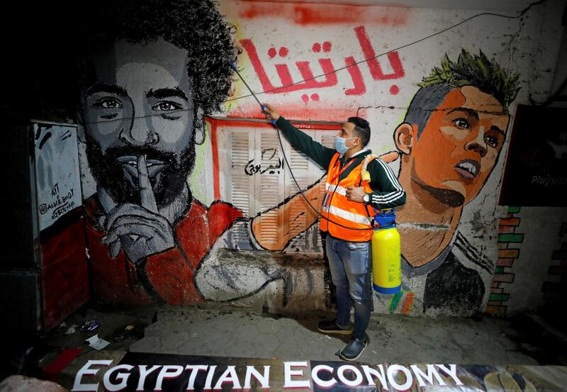 A volunteer sprays disinfectant on a wall, with a mural depicting football players Mohamed Salah and Cristiano Ronaldo, at Shubra El Kheima in Al Qalyubia, Egypt. Reuters