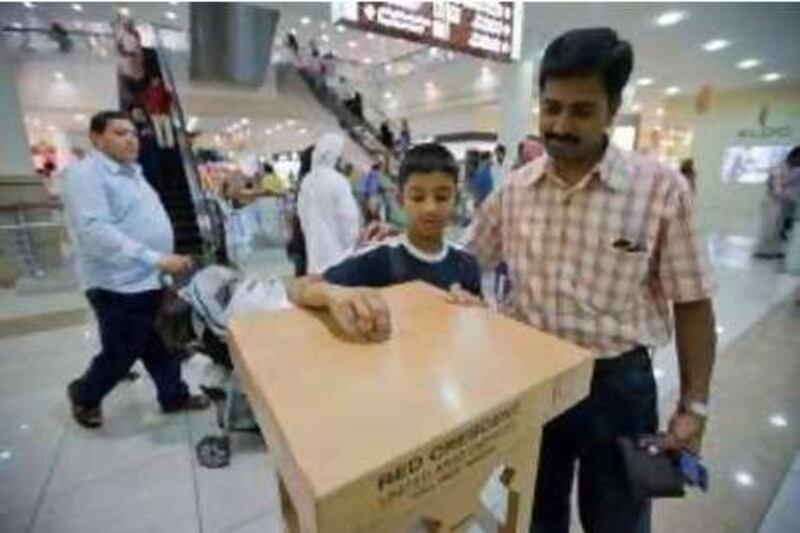 United Arab Emmirates - Abu Dhabi - Aug 29 - 2008 : Vijay Shashank,8, and his father Duraivel Shashank, from India, donate money in a Red Crescent collection box  in Al Wahda Mall as part of the Ramadan season. ( Jaime Puebla / The National ) *** Local Caption ***  JP103 - RED CRESCENT.jpg