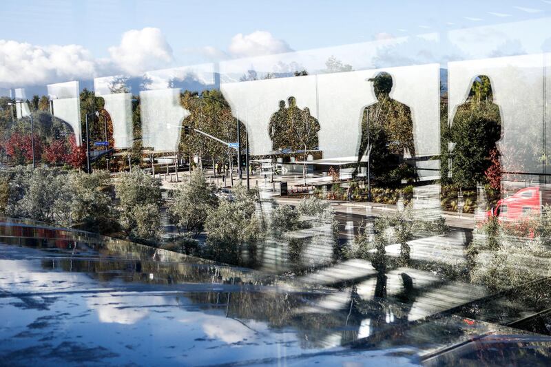 People are reflected in a glass wall on the roof top terrace at opening of the Apple Park Visitor Center on November 17, 2017 in Cupertino, California. (Photo by Amy Osborne / AFP)