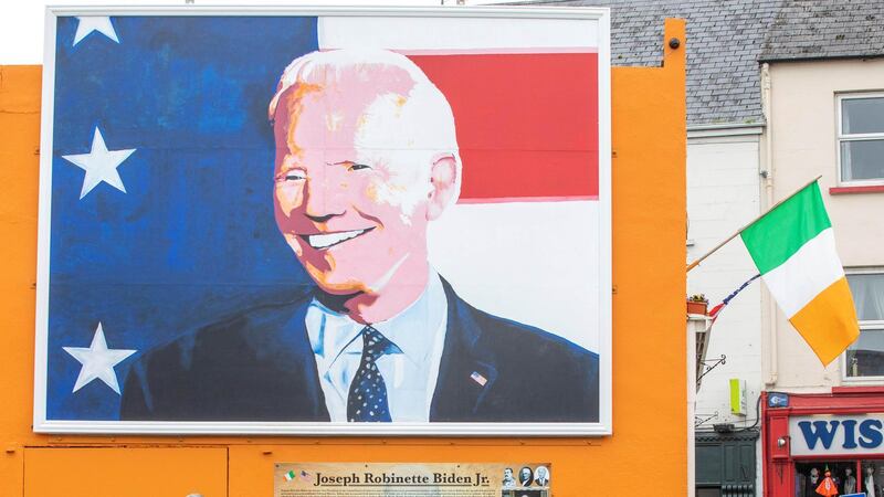 Pedestrians read an information board beneath a giant painting of US Presidential candidate Joe Biden, erected in his ancestral home of Ballina, north west Ireland, on October 7, 2020. - Thousands of miles east of the White House in Ireland, a pop-art portrait of US presidential candidate Joe Biden towers over his ancestral hometown of Ballina, County Mayo. In the town on Ireland's rugged Atlantic coast, the Democrat's distant relatives are thrilled to have one of their own bidding for America's highest office. "Obviously we're 100 percent behind Joe Biden," Laurita Blewitt, the former vice-president's third cousin, told AFP. (Photo by PAUL FAITH / AFP)