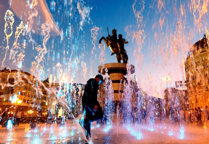 People play with water from a fountain near the "Warrior on a Horse" monument in Skopje, North Macedonia. Reuters