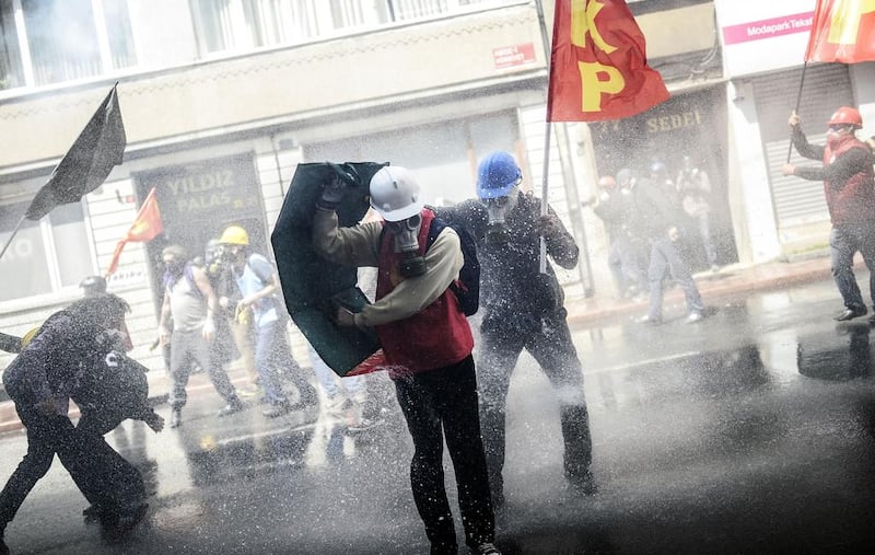 Protesters wearing gas and hard hats take cover as riot police use a water cannon to disperse a May Day rally in Taksim Square in Istanbul. Bulent Kilic / AFP / May 1, 2014
