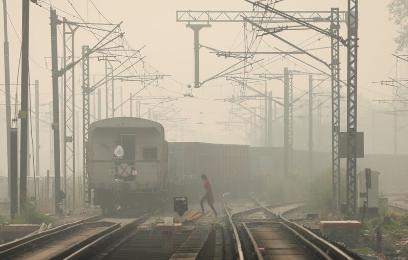 A woman crosses railway tracks as a goods train passes by, on a smoggy day in New Delhi. Reuters