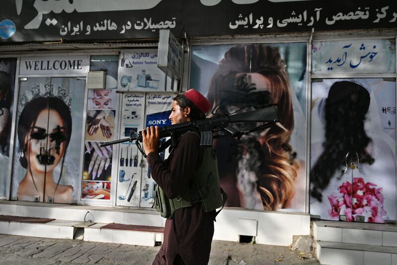A Taliban fighter passes a beauty salon in Kabul with images of women defaced with spray paint. AFP