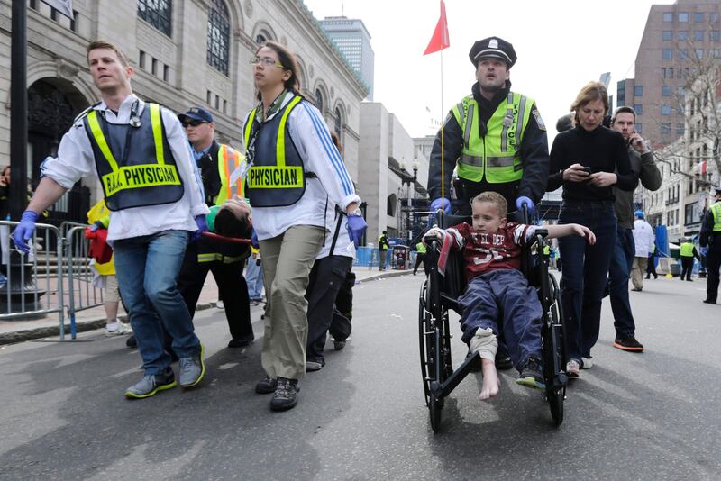 A Boston police officer wheels in injured boy down Boylston Street as medical workers carry an injured runner following an explosion during the 2013 Boston Marathon in Boston, Monday, April 15, 2013. Two explosions shattered the euphoria at the marathon's finish line on Monday, sending authorities out on the course to carry off the injured while the stragglers were rerouted away from the smoking site of the blasts. (AP Photo/Charles Krupa) *** Local Caption ***  Boston Marathon Explosion.JPEG-099dc.jpg