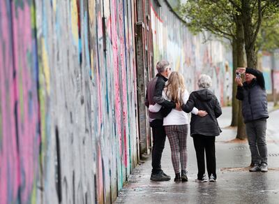 Tourists pose next to one of the 'peace walls' that still separate parts of Belfast. AP 