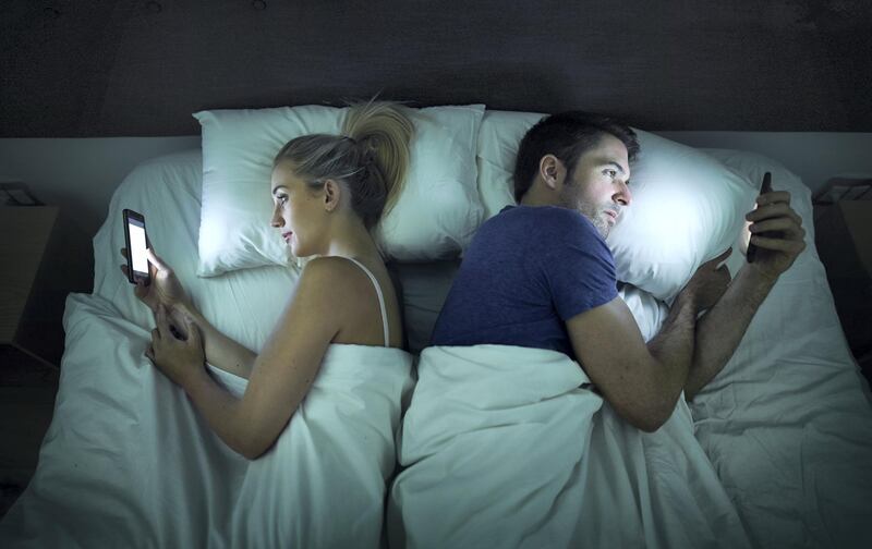 Shot of a young couple using their cellphones in bed at night back to back