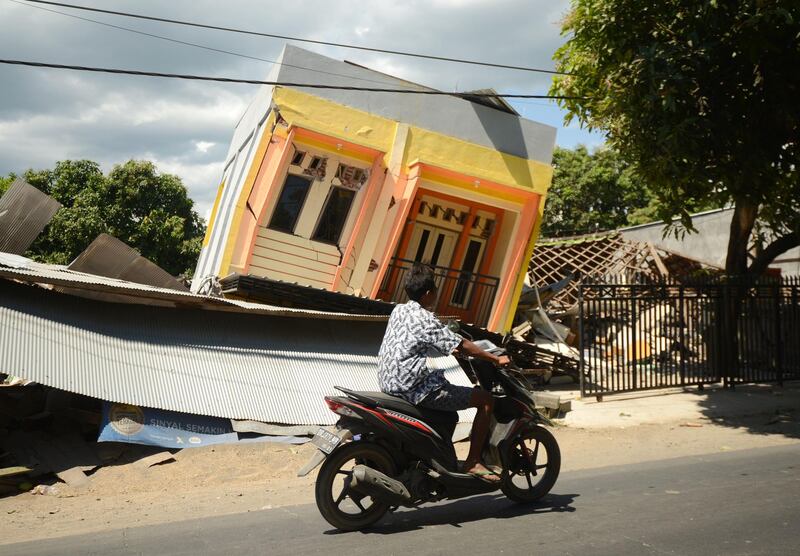 A man riding a motorcycle passes by a damaged house at Sira village in northern Lombok in West Nusa Tenggara province, two days after the area was struck by an earthquake. Sonny Tumbelaka/AFP