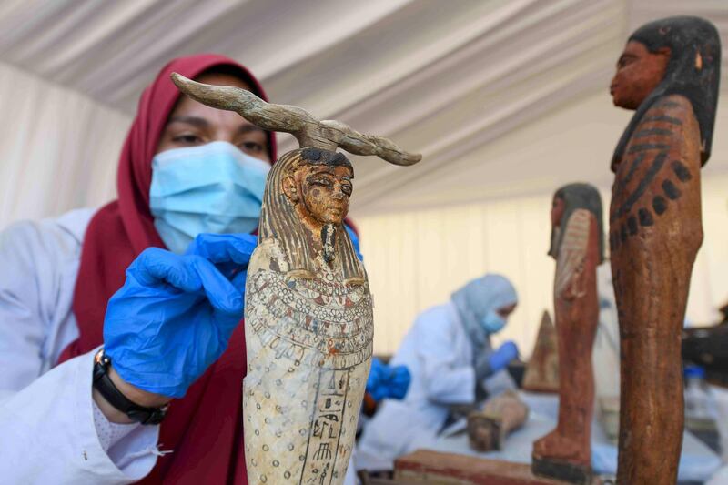 An archaeologist cleans a statue during the unveiling of an ancient treasure trove of more than a 100 intact sarcophagi. AFP