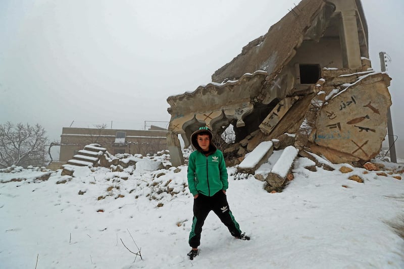 A boy stands next to a destroyed house covered in snow in Jabal Al Zawiyah, north-western Syria. The area is mostly deserted because of fighting and shelling. AFP