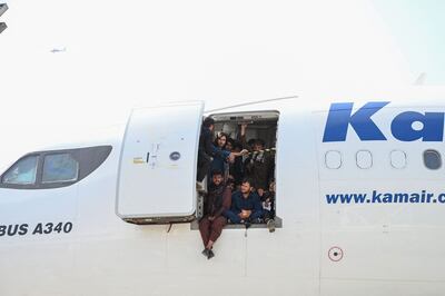 Afghan people climb up on a plane and sit by the door as they wait at the Kabul airport in Kabul on August 16, 2021. AFP