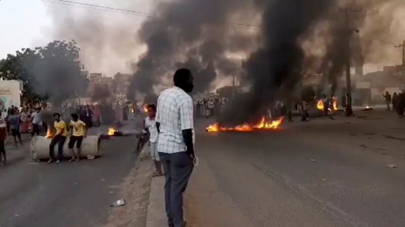 People gather on the streets of Khartoum as smoke rises after reports of a coup on Monday. Photo: Rasd Sudan Network / Reuters