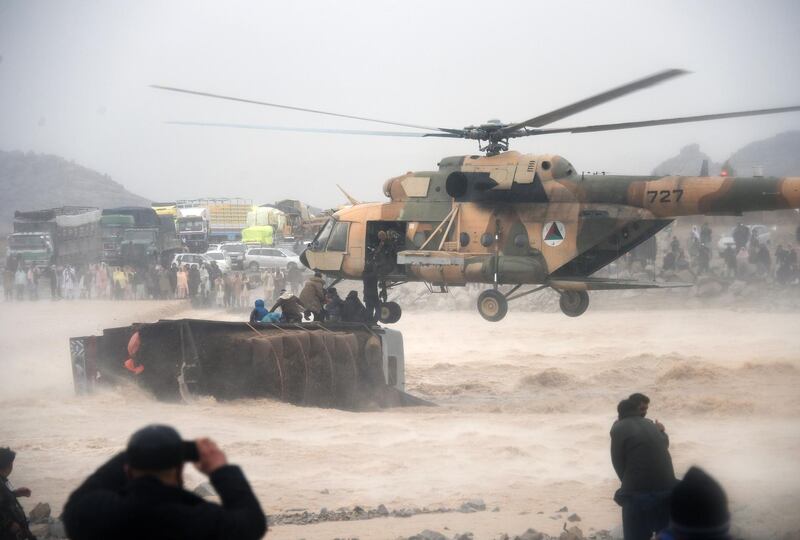 TOPSHOT - In this photo taken on March 2, 2019, an Afghan military helicopter rescues people from atop an overturned truck in flooded area of Arghandab district in Kandahar province. At least 20 people were killed by flash floods in southern Afghanistan's Kandahar province, the UN said on March 2, 2019, as heavy rains swept away homes and vehicles and potentially damaged thousands of houses. / AFP / JAVED TANVEER
