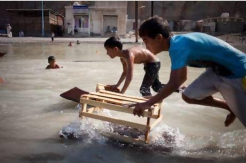 A group of young Kumzari boys cool off by playing and swimming with scrap pieces of wood in a small water hole. Razan Alzayani / The National