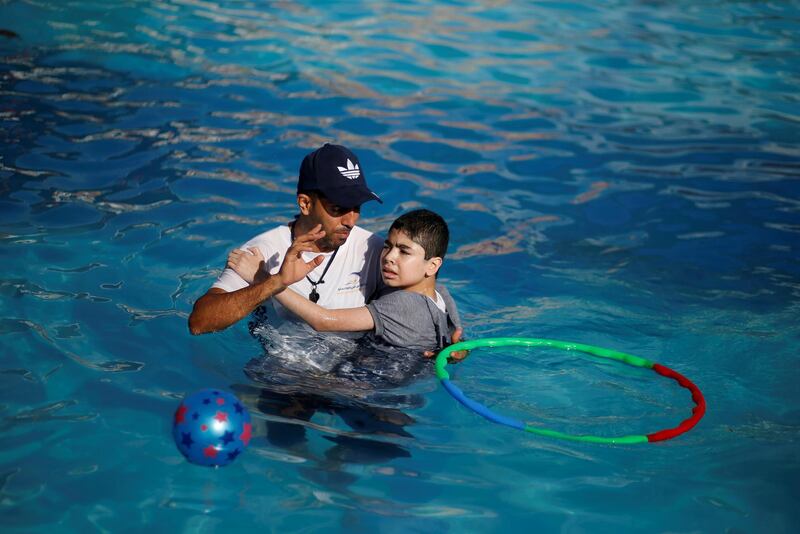 An autistic Palestinian boy is carried as he swims in a pool during a rehabilitation summer camp in the northern Gaza Strip. Reuters