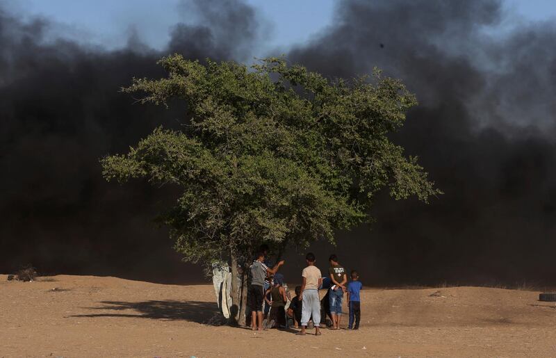 Protesters take cover behind a tree while others burn tires near the fence of the Gaza Strip border with Israel, during a protest east of Khan Younis, southern Gaza Strip. AP