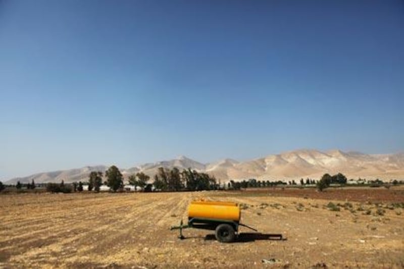 Elisha Zurgil, an adviser to the Israeli Fruit Growers' Association, ties up lush acacia trees on a kibbutz, front, while an empty water tank is left in a barren field in the Jordan River valley, above.