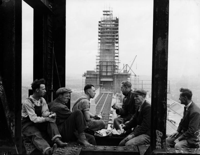 Construction workers take a lunch break with the 300ft high chimney of Battersea Power station, which was nearing completion, in the background in July 1932. Getty Images