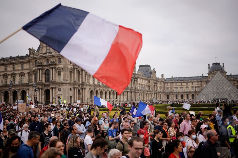 Protesters fly the French tricolour as they gather round the by the Louvre pyramid in Paris. They say coronavirus restrictions are contrary to the French tradition of liberty.