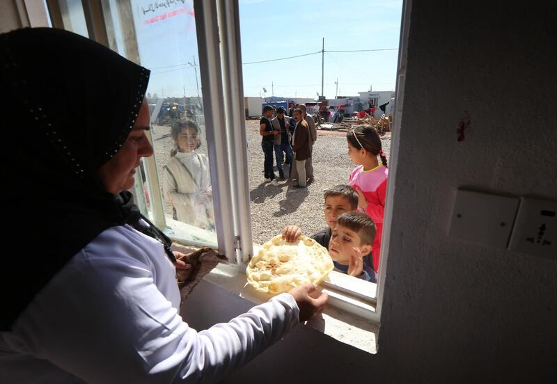 A volunteer from the Emirates Red Crescent distributes bread, made at a bakery run by the non-government organisation, to displaced Iraq children at the Harsham refugee camp where Iraqis, displaced due to attacks by Islamic State (IS) group militants, are taking shelter, ten kilometres west of Arbil, in the autonomous Kurdistan region of Iraq, on February 27, 2015. Some 900,000 internally displaced person's (IDP) have fled Iraq and found refuge in Kurdistan due to IS advances in the war-torn country. AFP PHOTO / SAFIN HAMED / AFP PHOTO / SAFIN HAMED