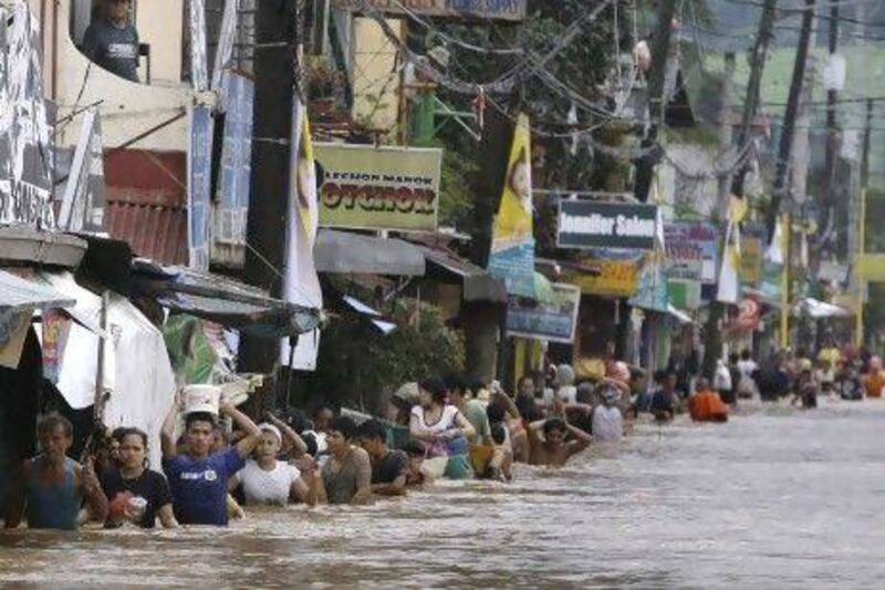 Residents attempt to cross a flooded road in Marikina City, east of Manila, yesterday. The floods have killed at least 23 people, battered a million others and paralysed the Philippine capital.