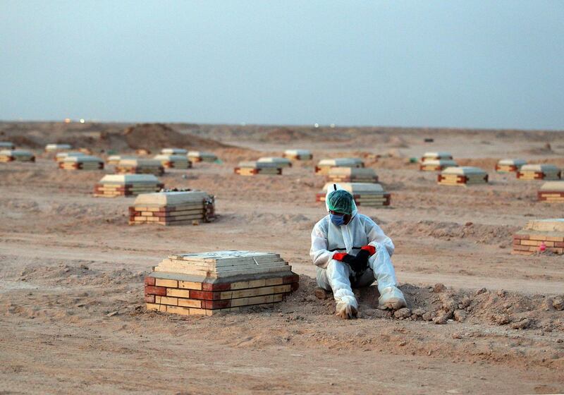 An Iraqi man in a hazmat suit mourns over a tombstone at a cemetery for COVID-19 victims, 20 km from the central Iraqi holy city of Najaf.   AFP