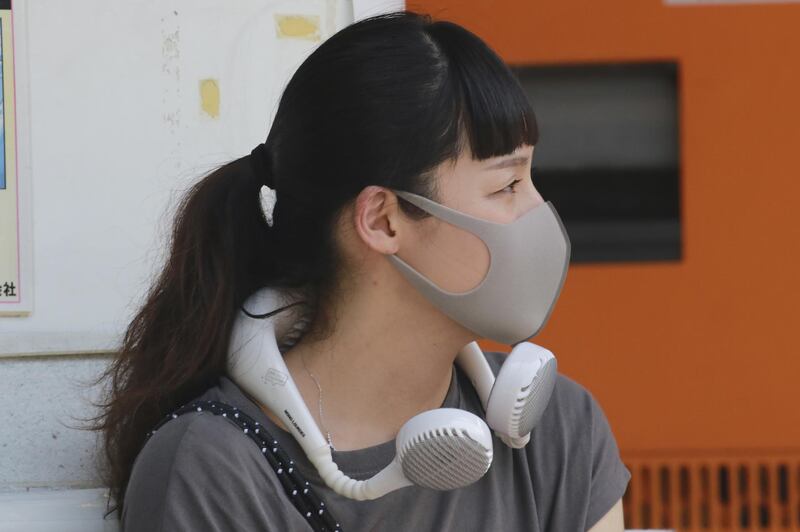 A woman wearing a face mask uses a portable fan around her neck to keep cool in the heat in Tokyo, Japan. AP Photo