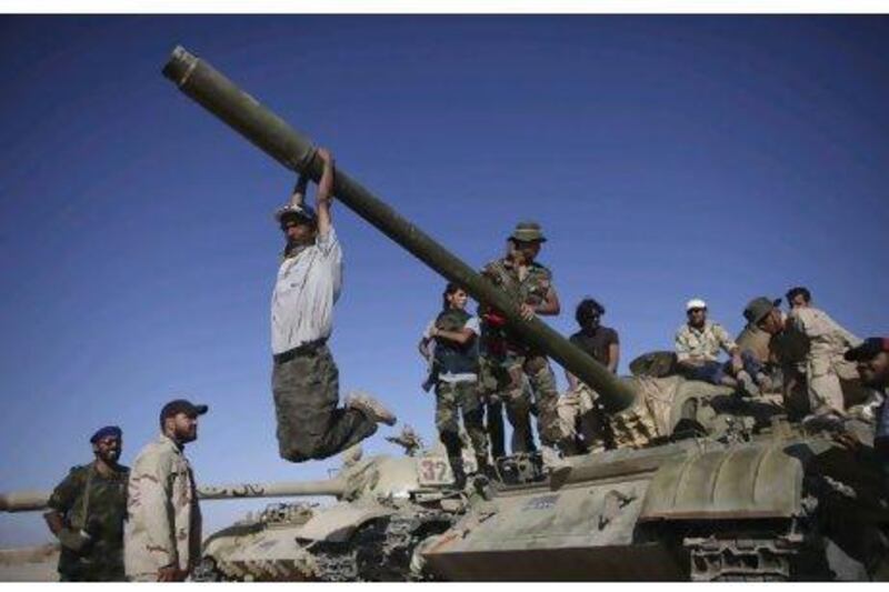 NTC fighters hang from the barrel of a tank in Wadi Dinar yesterday after NTC leadership claimed to have repelled pro-Qaddafi forces in the oasis city of Sabah.