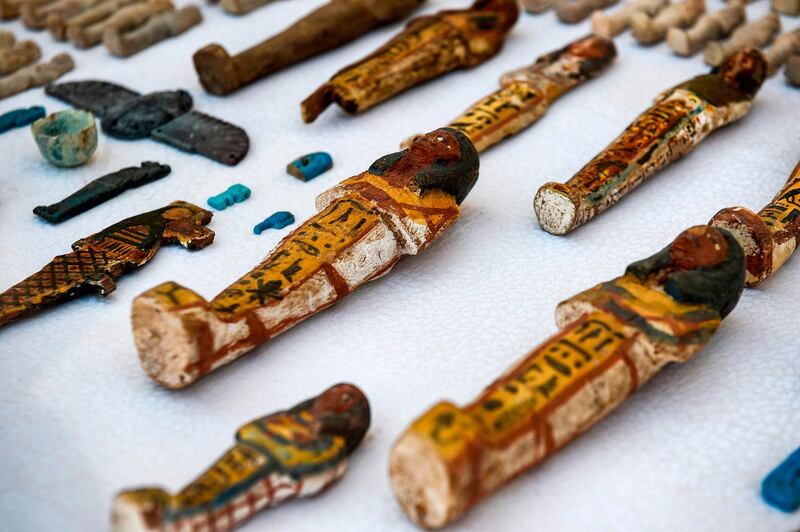 This picture shows carved wooden statues and funerary figurines called Ushabtis made of wood and clay laid out on a table. AFP