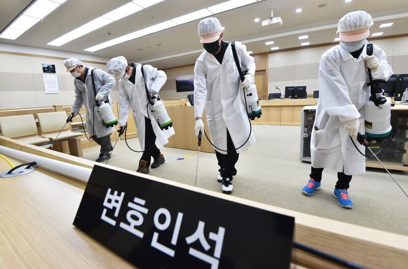 Workers wearing protective gear spray disinfectant as part of preventive measures against the spread of the COVID-19 coronavirus, in a courtroom at Suwon High Court in Suwon.  AFP