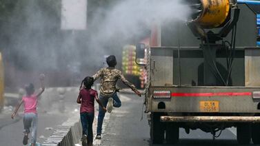 Children run behind a truck spraying water along a street on a hot summer day in New Delhi. AFP
