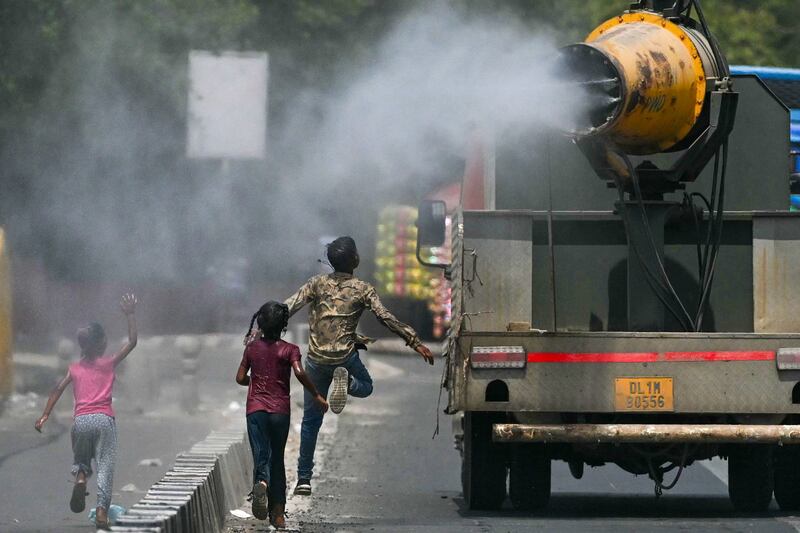 Children run behind a truck spraying water along a street on a hot summer day in New Delhi on May 28, 2024.  (Photo by Arun SANKAR  /  AFP)