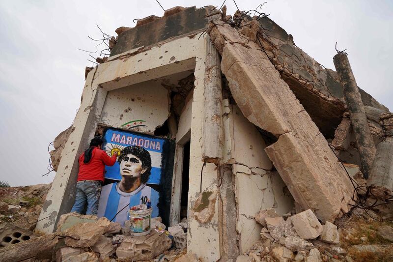 Syrian painter Aziz Asmar draws on the wall of a destroyed home a portrait of the late Argentine footballer Maradona in the town of Binnish in Syria's northwestern Idlib province. AFP