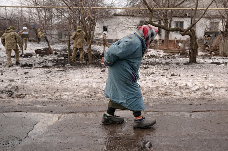 An elderly lady walks by as members of the Joint Centre for Control and Co-ordination survey damage to a house from artillery shell that landed in Vrubivka, eastern Ukraine. AP Photo