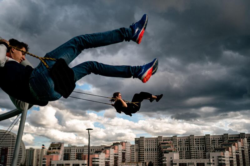 Teens swing on swings in a park in Moscow, with clouds in the sky.  AFP