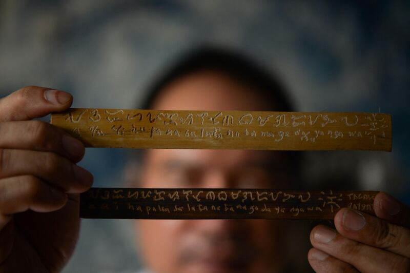 This photo taken on June 11, 2019 shows cultural advocate Leo Emmanuel Castro holding pieces of bamboo inscribed with indigenous Baybayin script at his shop in Manila.