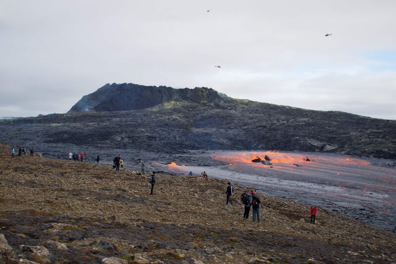 Tourists and other onlookers watch as lava flows from a tunnel near the crater in Geldingadalir valley, southwest of Iceland's capital Reykjavik on September 15, 2021.  - Slowly oozing at times, then spurting like a geyser and spitting rocks at others, a volcanic eruption near Reykjavik is still going strong six months after lava began flowing, Iceland's longest eruption since the 1960s.  While thousands of curious onlookers have been captivated by the mesmerizing spectacle playing out near Mount Fagradalsfjall since March 19 -- Iceland's sixth eruption in 20 years -- experts say a six-month eruption is not extraordinary.  Now officially named Fagradalshraun, or 'beautiful valley of lava' after the nearby Mount Fagradalsfjall, the volcano rose up from a fissure in the ground.  It has so far spewed out almost 143 million cubic metres of lava.  (Photo by Jeremie RICHARD  /  AFP)