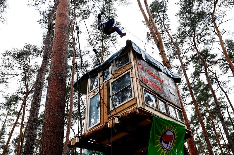 An activist uses a rope to climb over a tree house during a protest against deforestation, part of plans to extend the Tesla Gigafactory, in Gruenheide, near Berlin. EPA