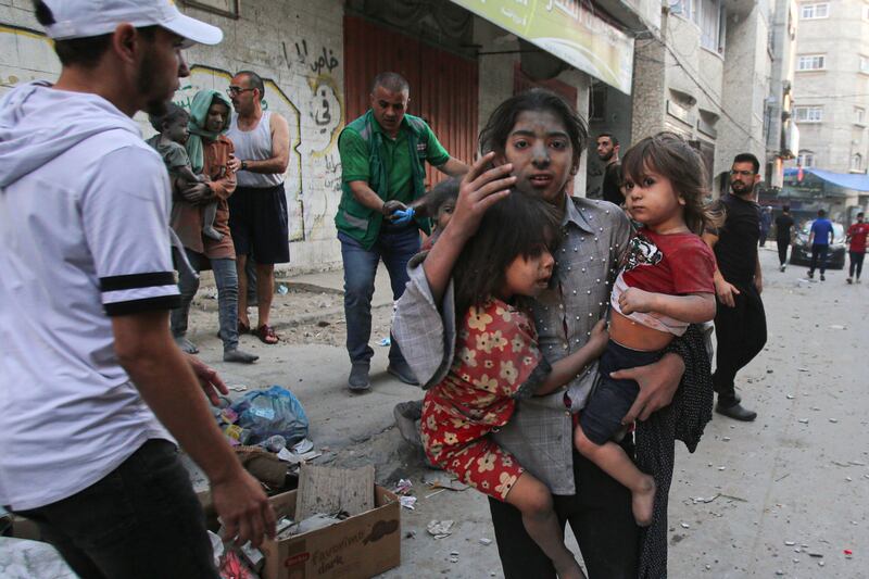 A Palestinian girl holds two children as she stands on a street in Gaza city as Israel continues to launch air strikes. AFP