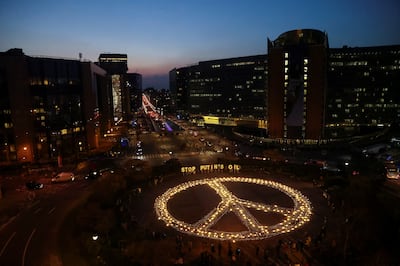 Demonstrators hold signs in front of a 'peace sign' lit outside the European Council during a protest to call on EU leaders to ban imports of Russian gas, amid Russia's invasion of Ukraine, in Brussels, Belgium on March 22, 2022. Reuters