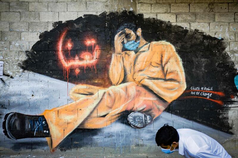 TOPSHOT - A youth, wearing a protective mask, walks past a mural reading "We are tired" in the Lebanese northern city of Tripoli on April 28, 2020. Lebanon is facing its worst economic crisis since the 1975-1990 civil war, now compounded by a nationwide lockdown to stem the spread of the coronavirus. The Lebanese pound has lost more than half of its value, and prices have soared.This is the case across the country, but Tripoli has been especially hard hit because more than half of its population had already been living at or below the poverty line. When mass protests erupted across Lebanon in October against perceived official graft and mismanagement, Tripoli fast became known as the "bride" of the street movement. / AFP / Ibrahim CHALHOUB
