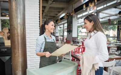 Friendly hostess working at a restaurant and talking to clients at the entrance. Getty Images