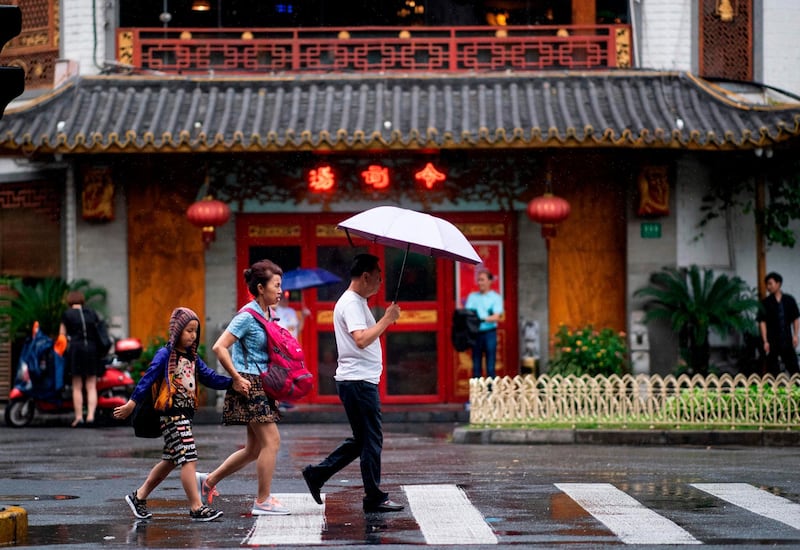 A man with an umbrella walks with his wife and child on a street on a wet day in Shanghai. AFP