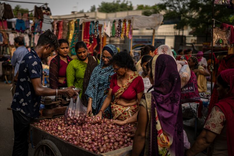 A roadside vendor packs onions in plastic bags as women shop at a weekly market in New Delhi, India. AP