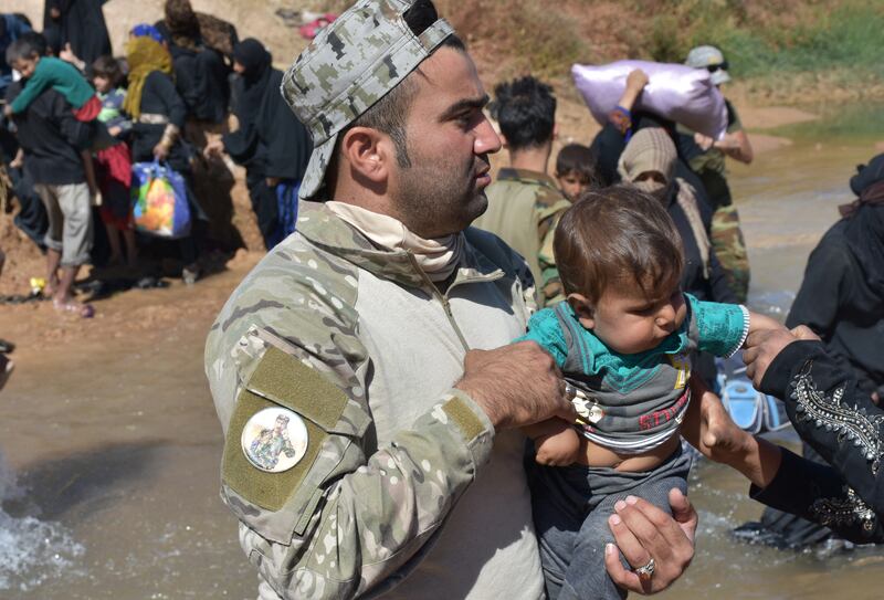 A fighter from the Hashed Al Sahaabi units helps displaced people who fled from battles to oust ISIS from Hawija cross a river in the area of Zarga, about 35km south-east of Kirkuk, on October 4, 2017.