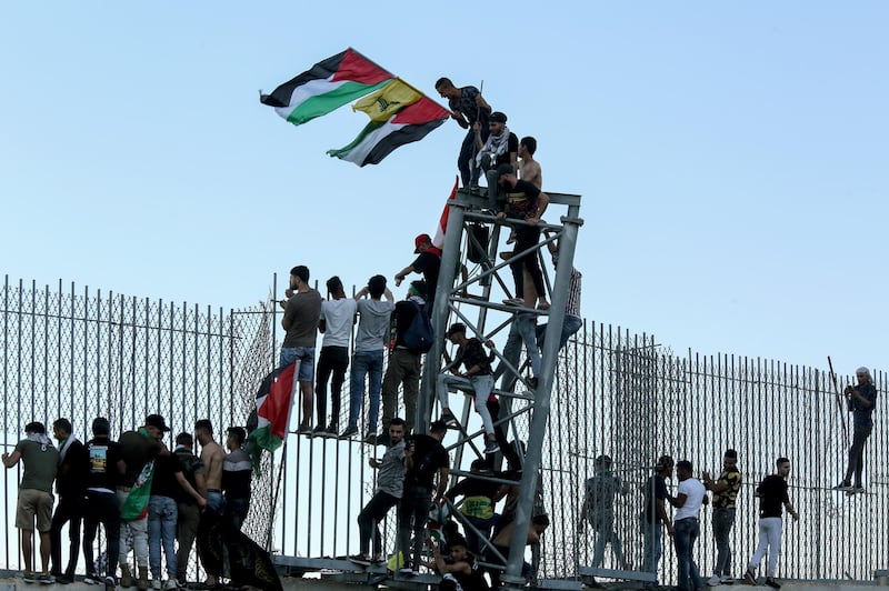 epa09202998 Supporters of Hezbollah and the Palestinian revolution faction climb the wall during protest at the Al Odaisseh area opposite the Al-Mutaleh Israeli settlement at the Lebanese border with Israel, 15 May 2021. People protested to support Palestinians following the past violence which has, according to local health authorities killed at least 139 people in Gaza and 7 in Israel.  EPA/NABIL MOUNZER