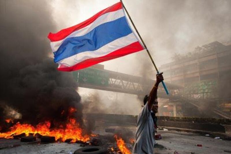 A Red shirt protester carries the Thai flag as tires burn and the violence in central part of the city escalates yesterday.