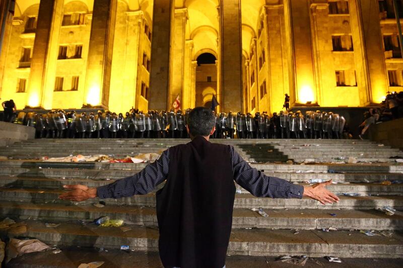 An opposition demonstrator stands in front of a police line at the Georgian Parliament to call for the resignation of the speaker of the Georgian Parliament in Tbilisi, Georgia, Friday, June 21, 2019. Police have fired a volley of tear gas at a massive throng of protesters outside the Georgian national parliament, who are trying to storm the building and are demanding the government's resignation.(AP Photo/Zurab Tsertsvadze)